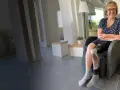 Lächelnde Frau mit Beinprothese sitzt im Sessel. Ihre Beinamputation ist gut versorgt, was die Pflegestufe unterstreicht.