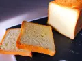 Pain de mie moelleux, parfait pour une recette pain de mie boulangerie maison. Deux tranches dorées et un pain entier sur un plateau sombre.