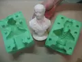 Making silicone molds for resin casting. A white bust is held between two green silicone molds, ready to capture its detail.