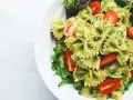 Pyszny makaron farfalle z aromatycznym pesto i soczystymi pomidorkami koktajlowymi, podany na liściach sałaty.