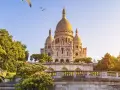 El barrio Montmartre, con la basílica del Sacré-Cœur al fondo, un carrusel y árboles frondosos bajo un cielo azul.