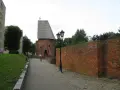Kamienna ścieżka prowadzi do zabytkowej baszty czarownic w Słupsku. Ceglana ściana i zabytkowa latarnia dopełniają malowniczy widok.