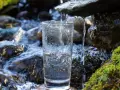 Ein Glas wird unter einem kleinen Wasserfall gefüllt. Die Frage, ob man quellwasser trinken kann, wird hier visuell beantwortet.