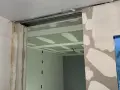 Ouverture dans un mur en cours de travaux de rénovation, avec plaques de plâtre et rails apparents.