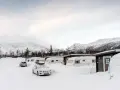 Vinterlandskap vid moskosel camping med snötäckta husvagnar och bilar, berg i bakgrunden.