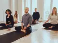 Menschen in einem hellen Raum meditieren auf Matten. Die Meditation wirkt beruhigend und fördert die Konzentration.