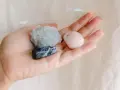 Mano sosteniendo tres piedras: una azul con vetas blancas, una azul pálido cristalina y una rosa pálido pulida. Son piedras para embarazadas.