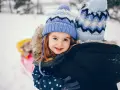 Uśmiechnięta dziewczynka w czapce i kurtce z gwiazdkami cieszy się zimowymi feriami, przytulając się do kogoś.