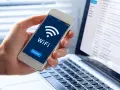 Dłoń trzyma smartfon z ikoną WiFi i napisem "Connect". Obok widać laptopa z listą e-maili, sugerującą pracę zdalną i dostęp do sieci, być może przez **ssid** domowy.
