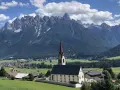 Chiesa con campanile rosso in primo piano, sullo sfondo le maestose vette delle Dolomiti e i **paesi più belli della Val Pusteria**.