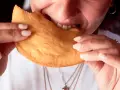 Close-up of a person biting into a golden-brown, fried pastry.