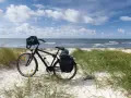 Rower z sakwami na plaży, gotowy do podróży trasą rowerową R10. Morze i niebo w tle.