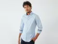 Uomo con camicia blu chiaro, dettagli floreali sui polsini e colletto. Un abbinamento elegante e moderno.