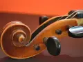 Drewniana ślimacznica skrzypiec, przypominająca spiralę, symbolizuje pierwsze instrumenty muzyczne i ich prostotę.