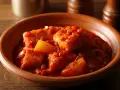 Bacalao a la vizcaina en cazuela de barro, con trozos de pimiento y cebolla en una salsa roja.