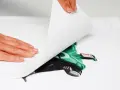 Manos aplicando una hoja para imprimir transfer sobre una camiseta blanca con un diseño de superhéroe verde.