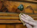 Restauración de mueble antiguo. Mano aplicando betún de judea antes y después, revelando su brillo natural.