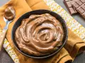 Una ciotola piena di deliziosa crema pasticcera al cioccolato, con una cucchiaiata pronta da gustare. Accanto, una tavoletta di cioccolato.