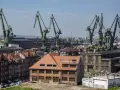 Widok na stocznię w Gdańsku z charakterystycznymi dźwigami. W oddali budynek z napisem "Nowe Syrie", nawiązujący do muzeum sztuki współczesnej Gdańsk.