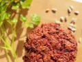 Pyszne kotlety z buraka, przypominające falafel, leżą na desce obok gałązki pietruszki i nasion słonecznika.