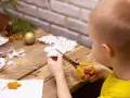 Małe rączki wycinają śnieżynkę z papieru. Na stole leżą gotowe ozdoby i gałązka choinki.