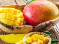 Soczyste, pokrojone w kostkę i w całości mango w drewnianej misce. Owoc ten zawiera mnóstwo witamin.