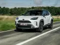 Biały Yaris Cross Hybrid jedzie po drodze, otoczony zielenią.