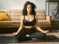 Frau in schwarzer Sportkleidung praktiziert Meditation für tiefe Entspannung auf einer Matte vor einem karierten Sofa.