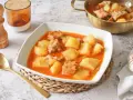 Un reconfortante plato de patatas con costillas en una salsa rojiza, servido en un cuenco blanco.