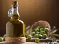 Bottiglia di olio extravergine d'oliva accanto a olive verdi, per capire la differenza tra olio di oliva e olio extravergine.