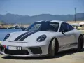Szary Porsche 911 z czarnymi pasami, stojący nad wodą. Zastanawiasz się nad porsche 911 cena?