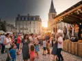 Gente bailando en una plaza adoquinada durante la fiesta de la música en Francia. Una banda toca en un escenario iluminado, con edificios históricos y una iglesia al fondo.