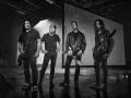 James Hetfield und Metallica im Jahr 2000, bereit für die Bühne. Die Bandmitglieder stehen in dunkler Kleidung, einige mit Gitarren.