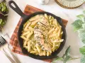 Deliciosa pasta con pollo en sartén, cubierta con hierbas frescas. Acompañada de una ensalada verde y tenedores.