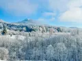 Bieszczady zimą. Ośnieżone drzewa i góry pod błękitnym niebem. W oddali widać mały domek.