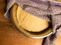 Ein geschmeidiger Teig ruht in einer Schüssel, bedeckt mit einem karierten Tuch, bereit für das Backen.