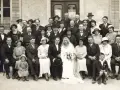 Un groupe pose pour une photo de mariage, peut-être pour un registre mariage. La mariée porte une robe blanche et un voile.