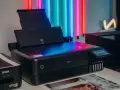 Czarna drukarka Epson z kolorowym ekranem, idealna do drukowania zdjęć. Obok stoi starszy model.