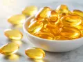 Capsule dorate piene di olio, che ricordano le proprietà omega 3, in una ciotola bianca e sparse sul piano.