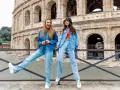 Dwie kobiety w jeans total look pozują przed Koloseum. Jedna ma rozpuszczone włosy i szeroki uśmiech, druga w kapeluszu bucket hat.