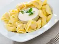 Pyszne pierożki tortellini w sosie śmietanowym, udekorowane natką pietruszki. Idealne danie na szybki obiad.