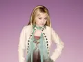 Miley Cyrus jako Hannah Montana w białej kurtce i turkusowym szalu, z błyszczącymi kolczykami.