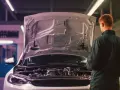 Meccanico esamina il motore aspirato di un'auto con il cofano aperto in un'officina.