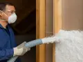 Operaio con maschera e occhiali insuffla materiale isolante. Attenzione: la lana di vetro è infiammabile.