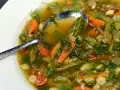 Un fumante minestrone di verdure, ricco di carote, fagioli e erbe aromatiche, servito in una ciotola bianca con un cucchiaio.