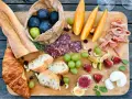 Tabla de quesos y embutidos: baguettes, croissants, higos, uvas, melón, jamón serrano y salami. Un festín que muestra qué comen los franceses.