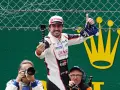 Fernando Alonso celebra su victoria en Le Mans, con una gorra y un trofeo. Fotógrafos capturan el momento.