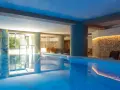 Indoor swimming pool with lounge chairs and a stone wall with warm lighting.