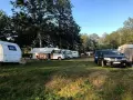 Solig dag på Alsterbro camping med husvagnar, husbilar och bilar uppställda på gräset.