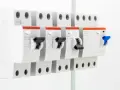 Rząd białych wyłączników nadprądowych, każdy z czerwonym elementem i czarnym przełącznikiem. To zabezpieczenie przedlicznikowe zapewnia bezpieczeństwo instalacji elektrycznej.